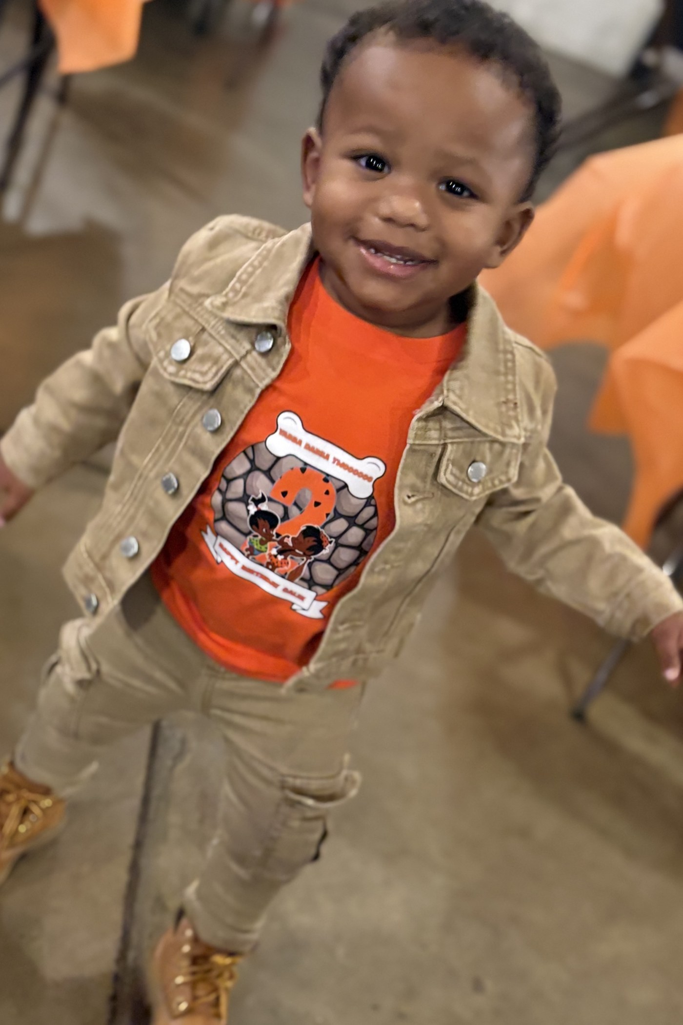 A custom orange birthday shirt handmade by LL Cool Crafts, worn by a smiling toddler at his second birthday party